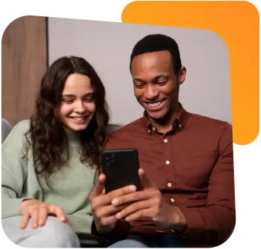 Casal sorrindo enquanto usa um laptop em casa, sentado em um sofá.