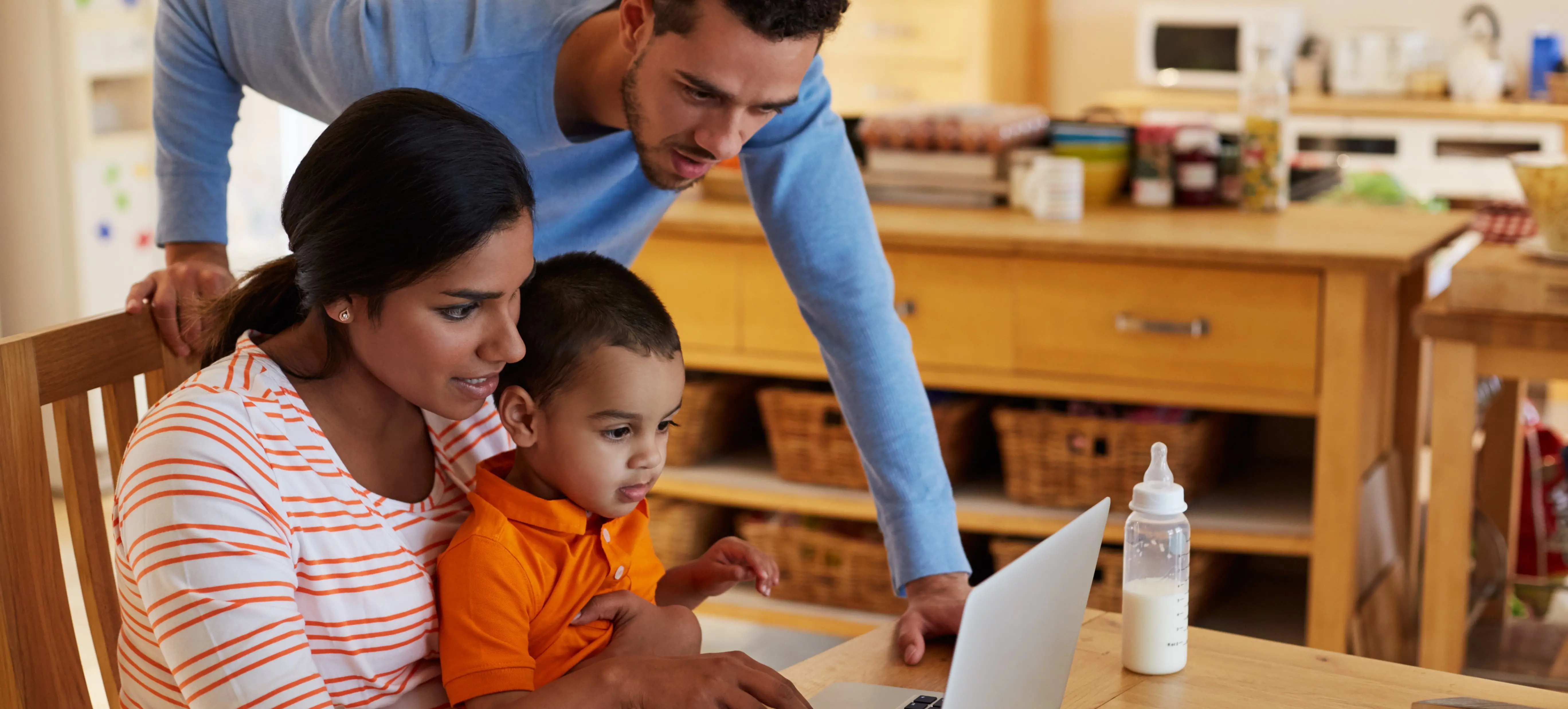 Um casal com o filho em uma casa pesquisando informações no notebook 